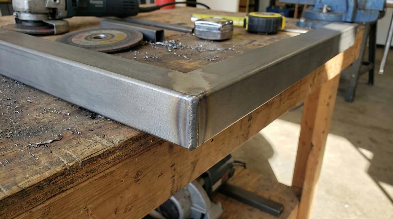 A clean MIG-welded joint on a square steel tube railing on a workshop bench
